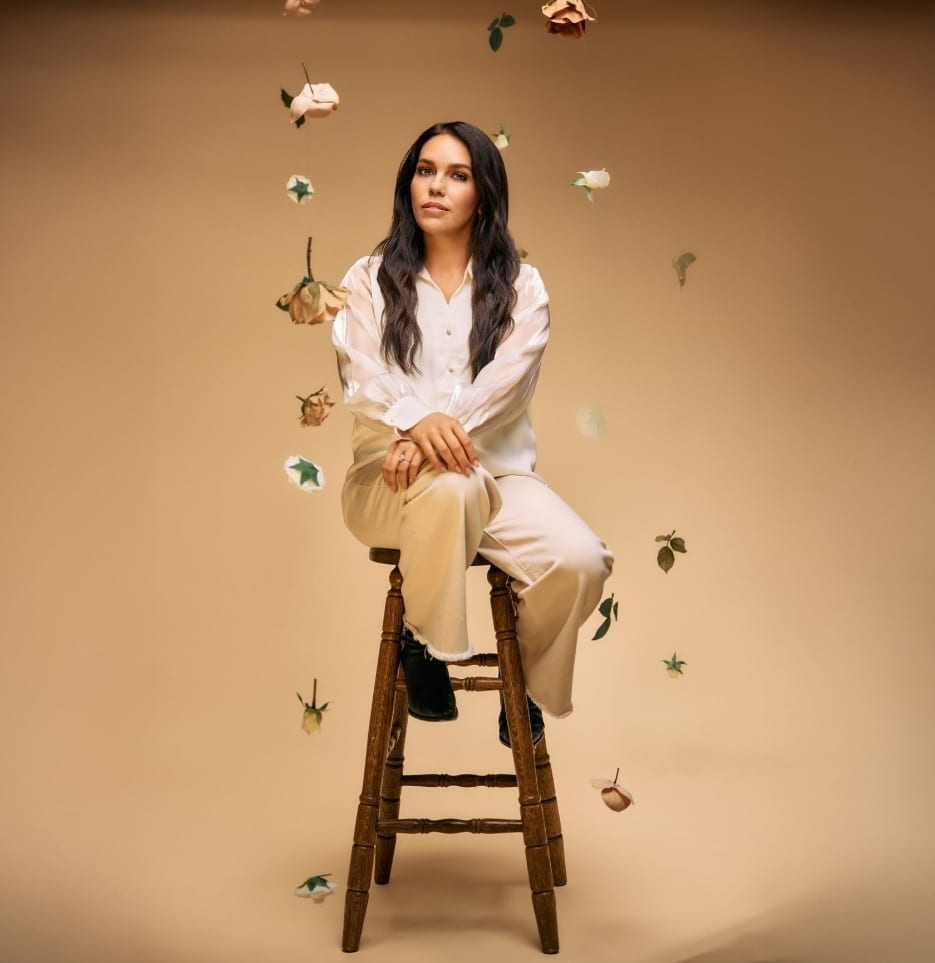 Melody Noel Altavilla seated on a stool, roses falling around her